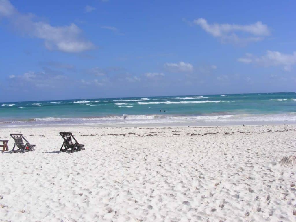 A beach view with an empty beach chair facing the water