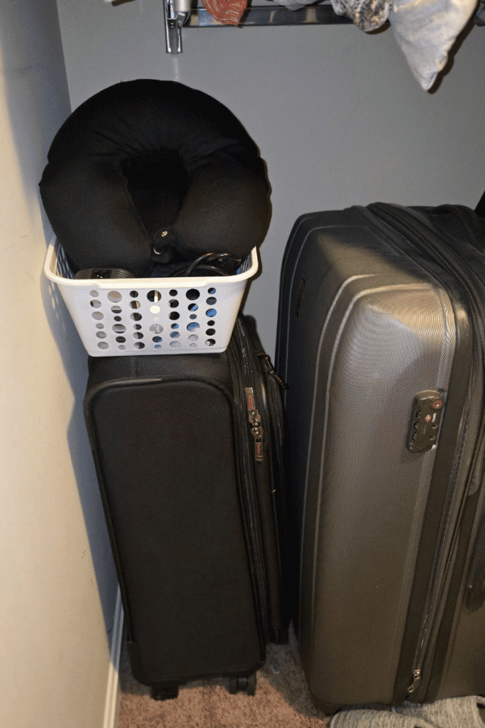Cruise prep pre-pack section in a closet with suitcase, laundry basket, and travel pillow ready for packing before a cruise.