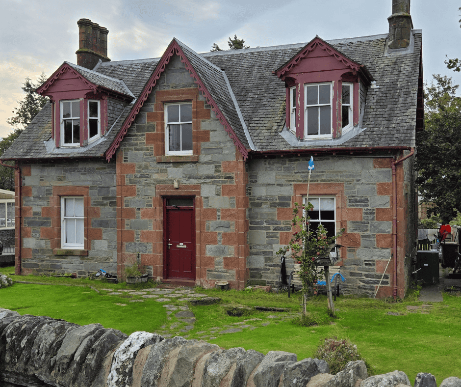 Stone cottage in the British Isles with red trim and green lawn on a sunny day