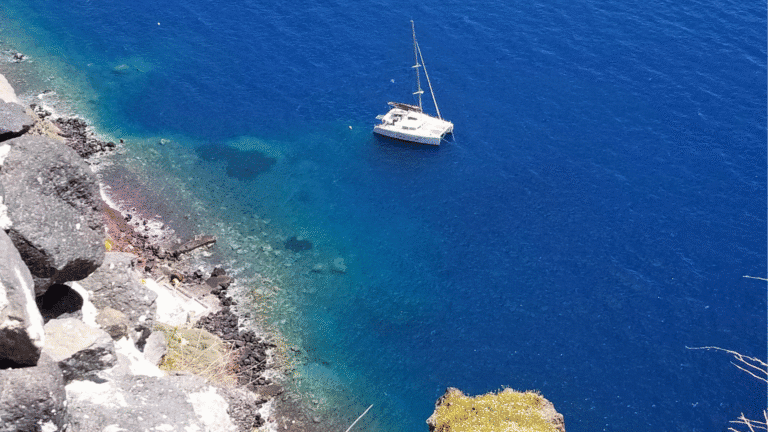 Sailboat anchored in the bright blue waters off the rocky coastline of Greece: dreamy view perfect for a European cruise preparation checklist.