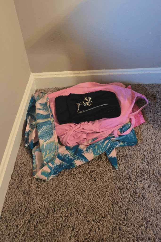 Cruise prep pre-pack pile in the corner with folded clothes and travel bag set aside before packing for a cruise.