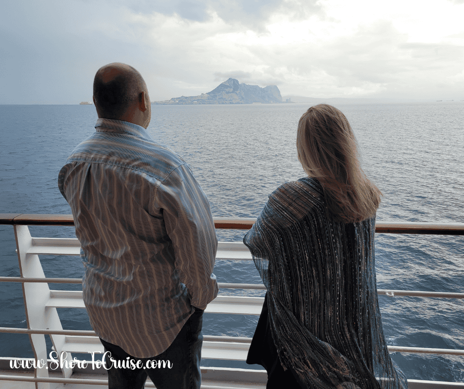 Couple standing on a cruise ship deck looking out to sea, dressed in light layers for a cool Northern Europe evening.