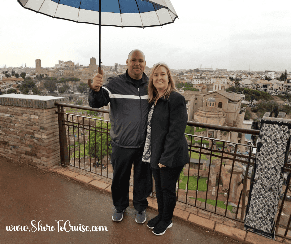 Cruise travelers visiting the Colosseum in Rome on a spring day with light jackets and an umbrella — a reminder to pack a rain jacket for Mediterranean weather.