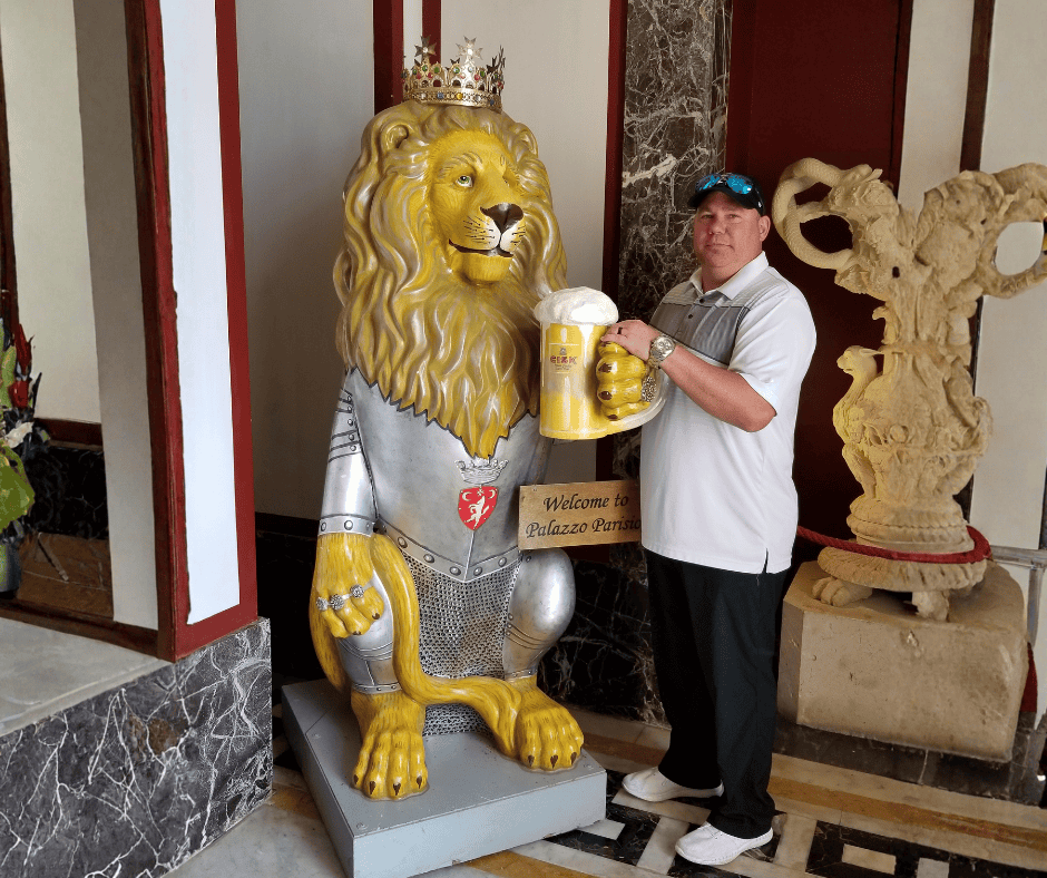 Cruise traveler posing with lion statue and beer mug at Palazzo Parisio in Malta — casual cruise outfit with polo and loafers perfect for port days.
